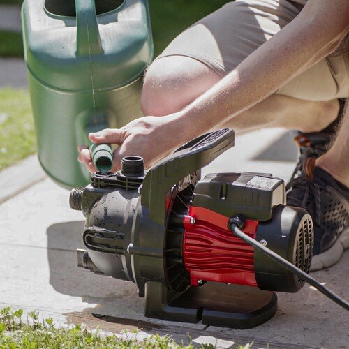Mit einer Gießkanne wird Wasser in eine Gartenpumpe eingefüllt
